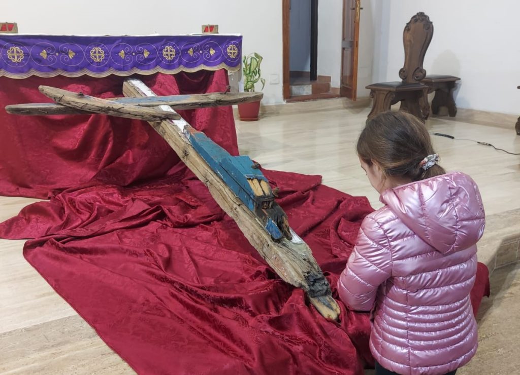 bambina prega davanti alla croce costruita con i resti del barcone naufragato a Cutro